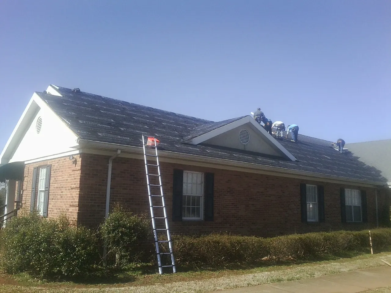 Crew tearing shingles off a brick ranch roof with a ladder set — Emergency Roof Repair work by our crew in Cliff Island