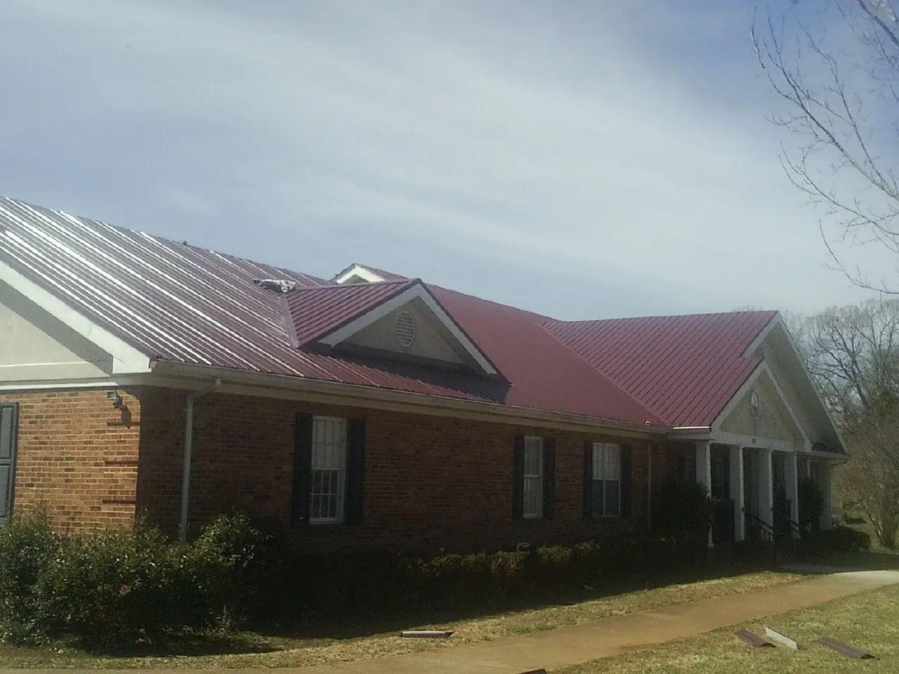 Red metal roof with gabled entries on a long brick building, from a Hail Damage Roof Repair job in Cliff Island