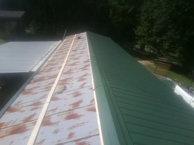 Old rusted panels beside newly installed green metal roofing — Wind Damage Roof Repair by Roofing Brothers in Cliff Island