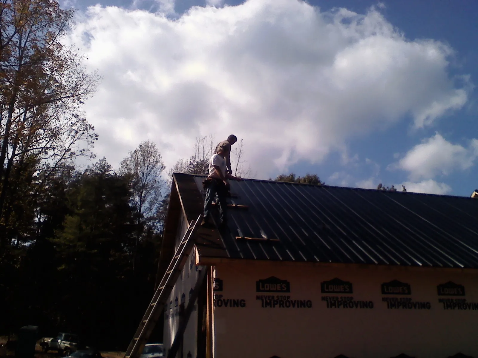 Roofer fastening dark metal panels high against a cloudy sky, from a Roof Inspection job in Cliff Island
