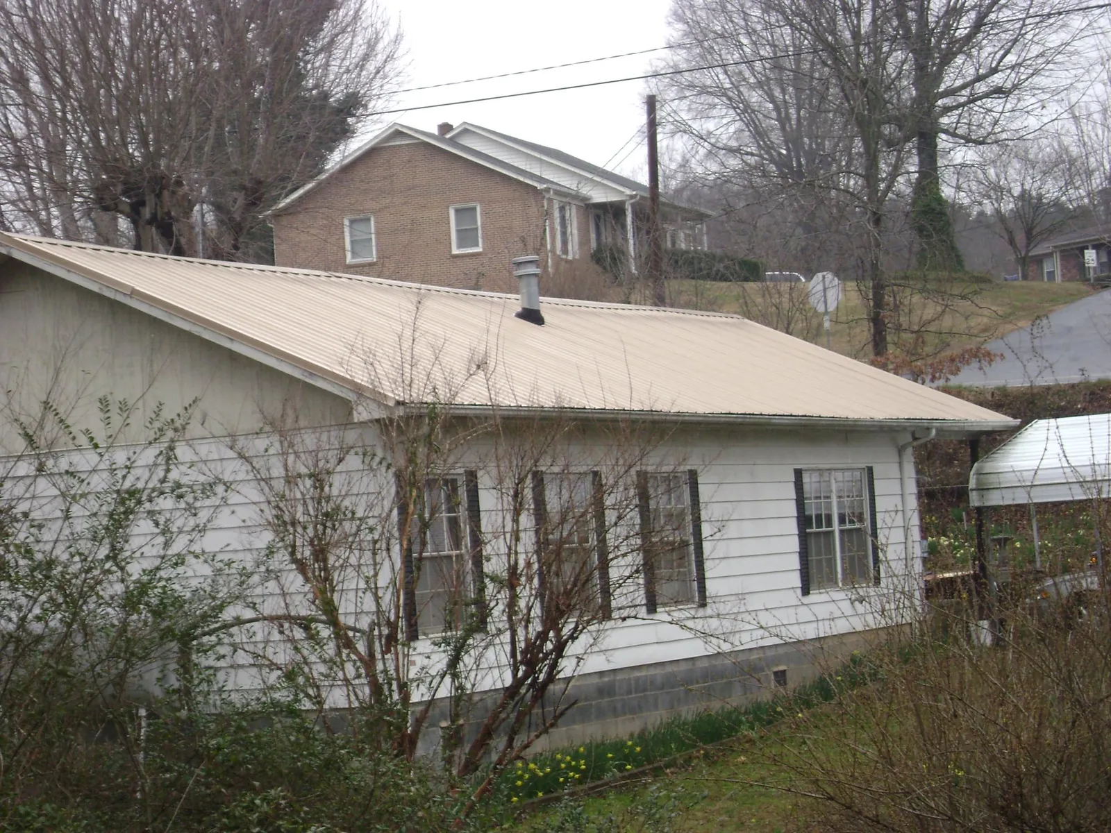 Tan metal roof on a white sided house set into a hillside — Commercial Roofing by Roofing Brothers in Cliff Island